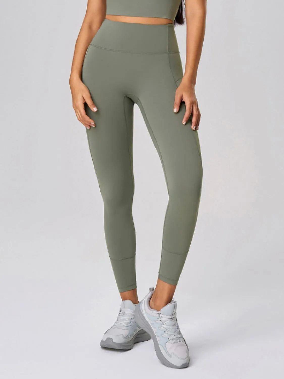 Model wearing olive green high-waist active leggings with a smooth fitted silhouette, ankle-length hems, and subtle seam construction.