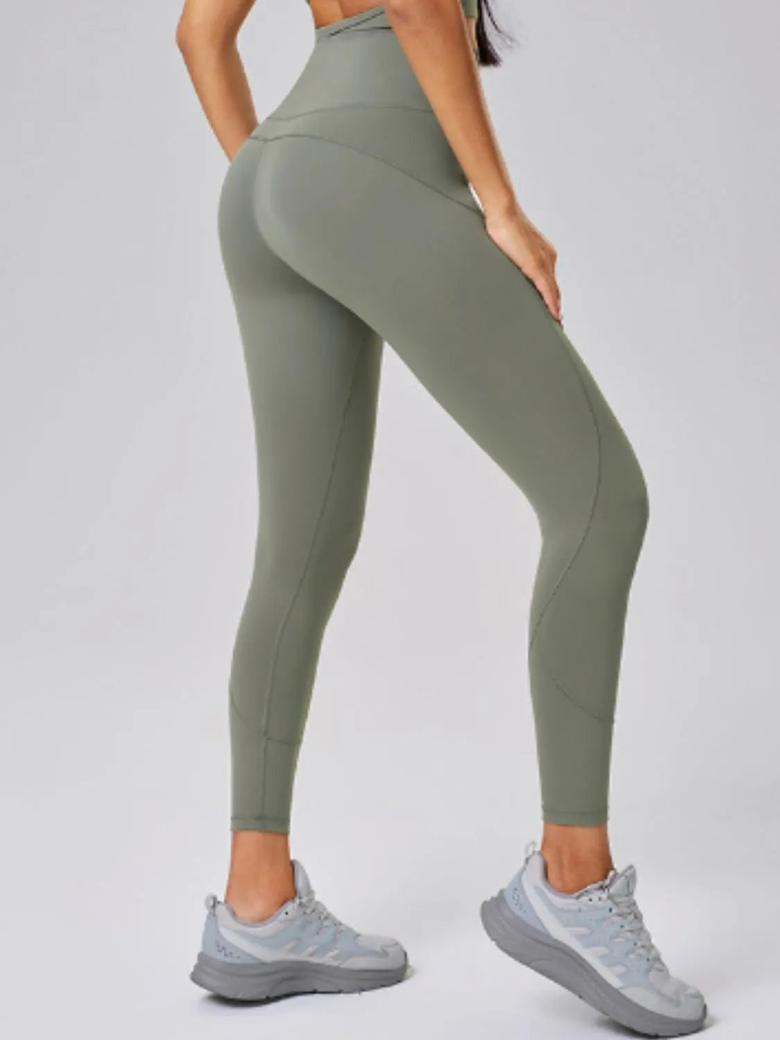 Model poses in sage green high waist active leggings, showing a fitted full-length silhouette with curved seam construction and moderate stretch.