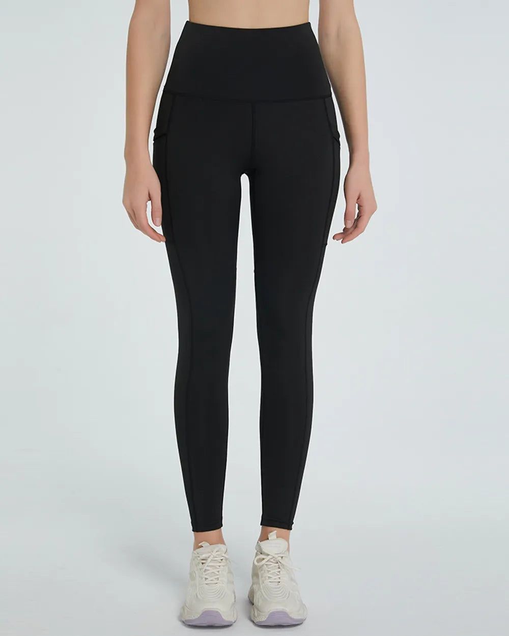 Model stands facing forward in black high-waist active leggings with a smooth waistband, fitted tapered silhouette, and subtle side seam detailing.
