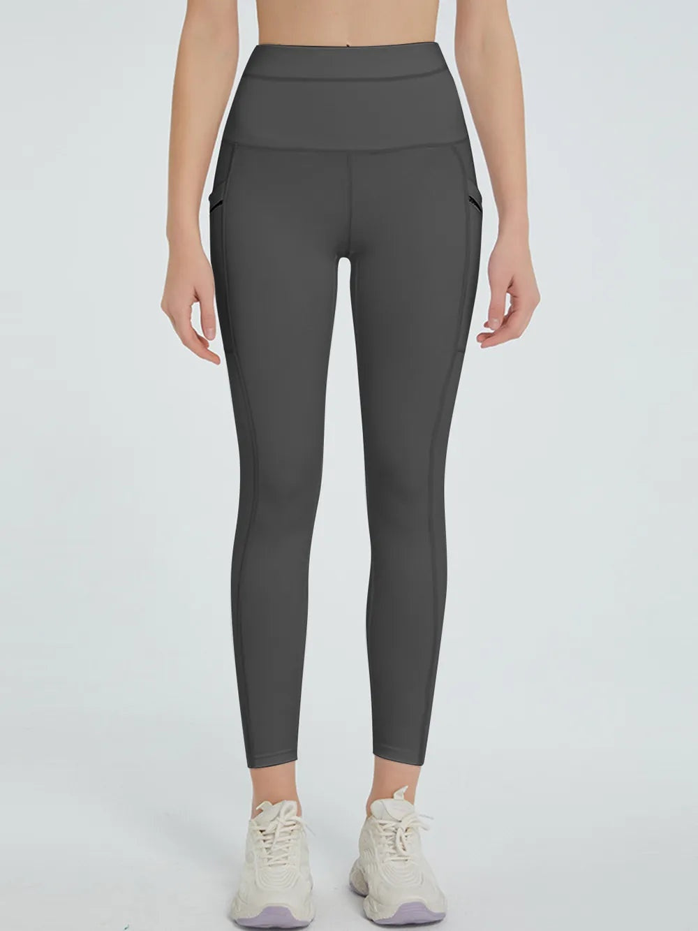 Model stands facing forward in dark gray high-waist active leggings with a fitted, tapered silhouette and visible seam construction along the legs.