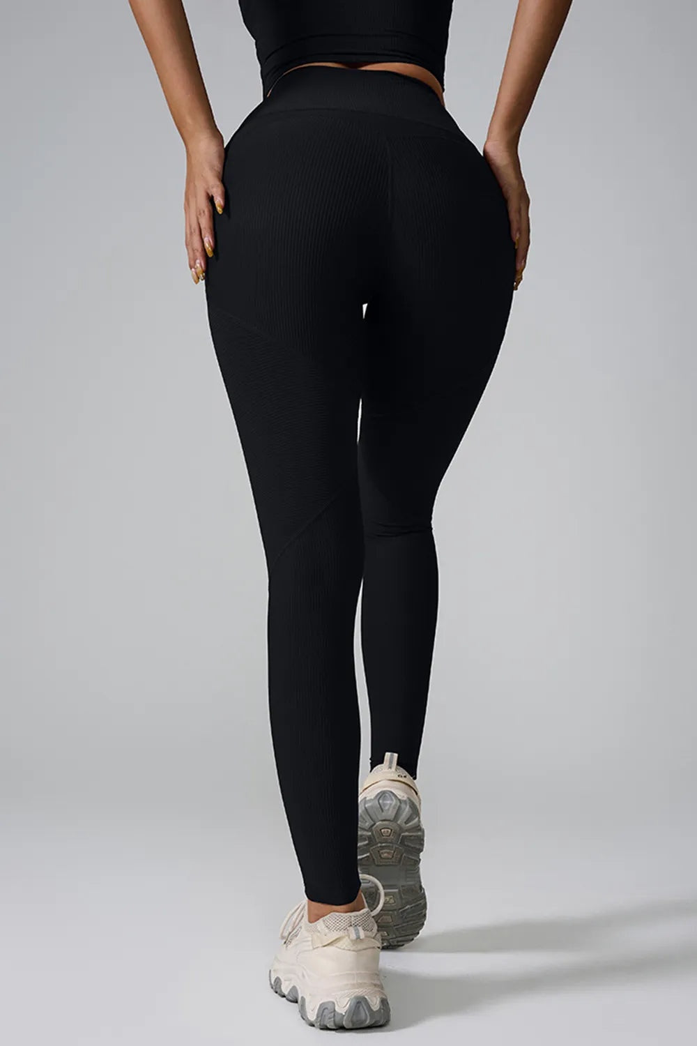 Model poses from the back in black high-waist active leggings with a sleek, stretchy fitted silhouette and ankle-length construction.
