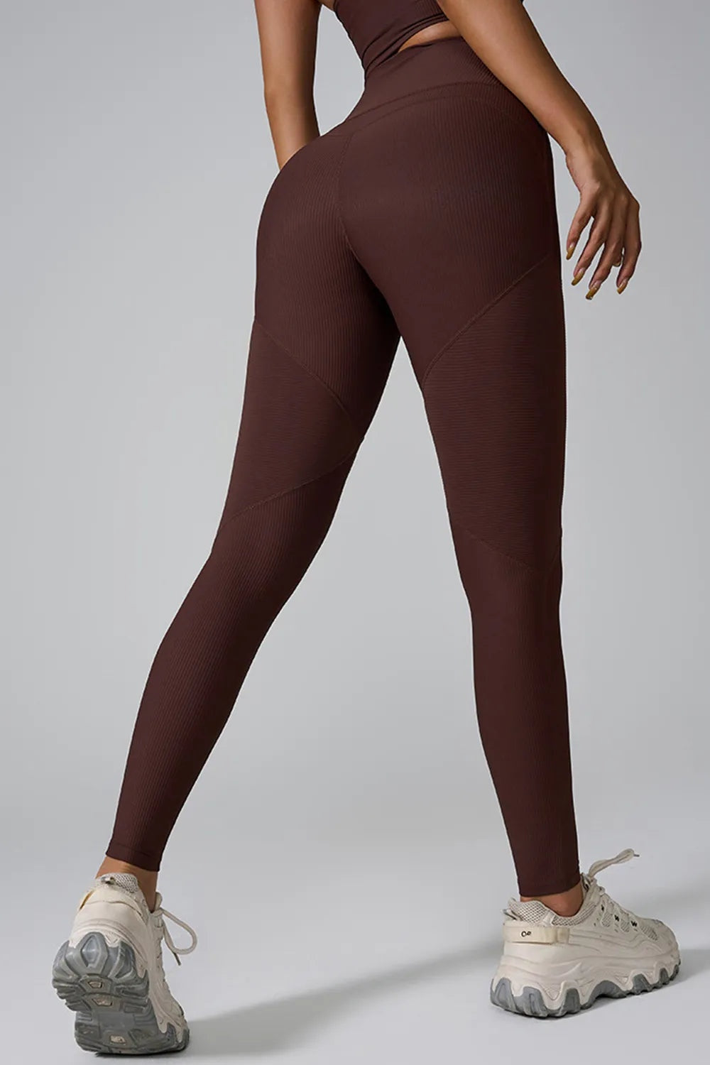 Model poses in brown high-waist active leggings with a snug full-length silhouette, ribbed texture, and diagonal seam detailing.