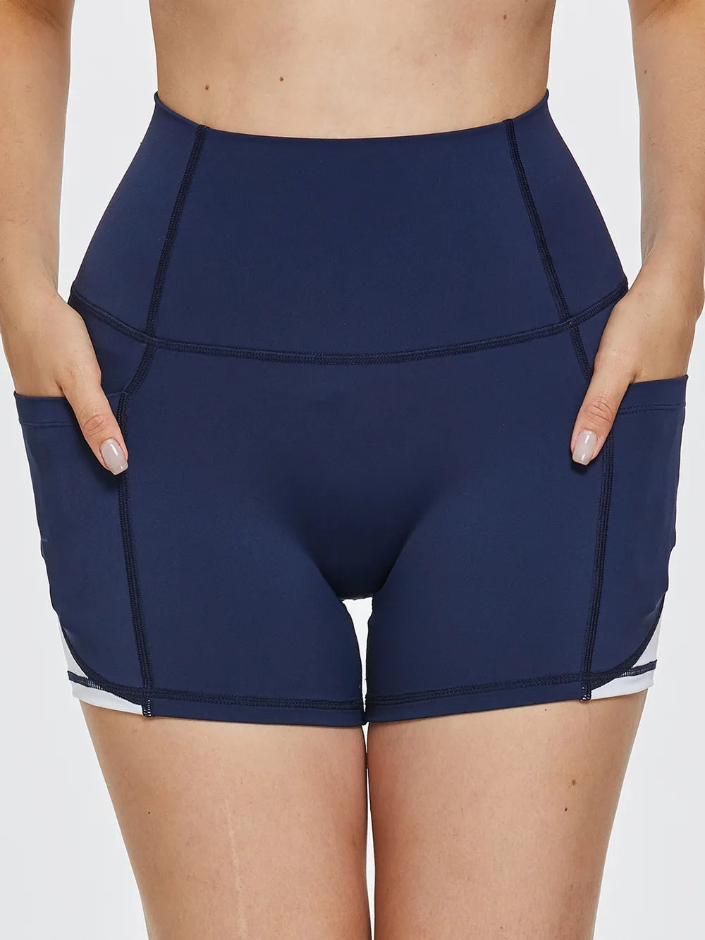 Model wears navy high-waist active shorts with a fitted compression silhouette, contrast seam construction, and side pockets, shown from the front.