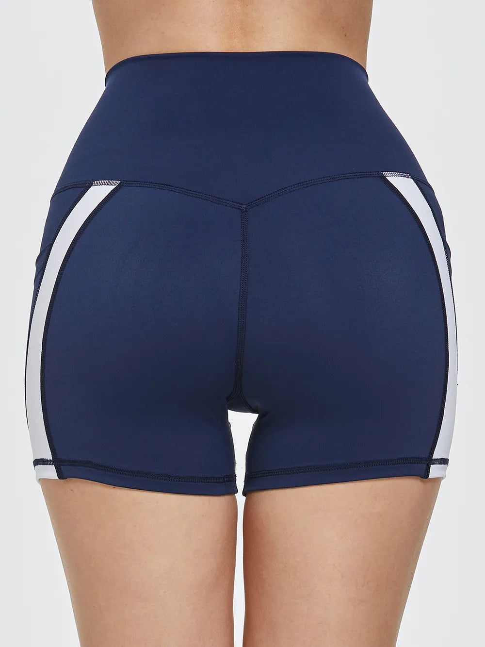 Rear view of a model wearing navy high-waist active shorts with a fitted silhouette, white side panels, and visible contrast stitching.