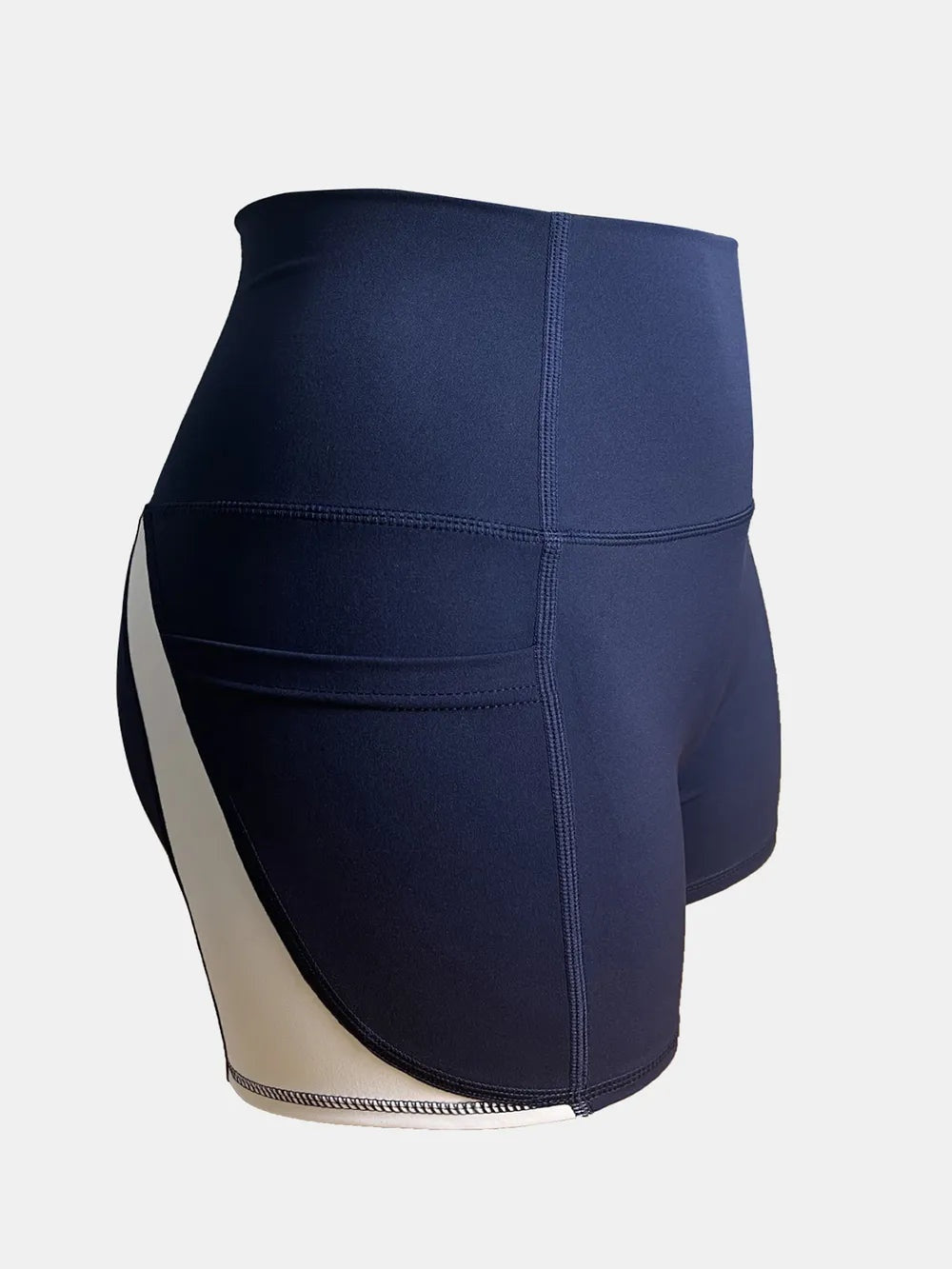 Navy high-waist active shorts feature a fitted, stretchy silhouette, wide waistband, contrasting side panel, and visible stitched seams.