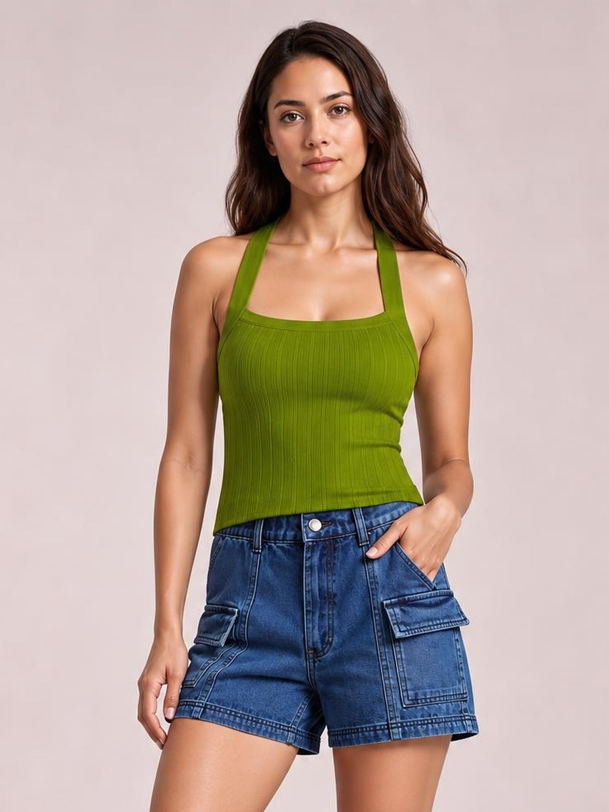 A woman modeling a ribbed olive green halter tank top paired with blue denim cargo shorts, set against a solid light beige studio background.