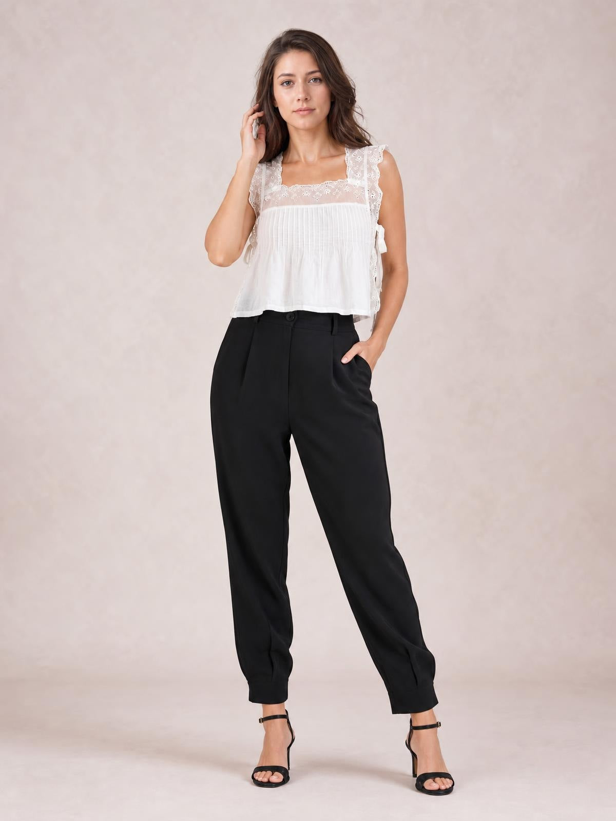 A model poses in black high-waist cropped pants with a front button, side pockets, and a relaxed tapered silhouette, one hand tucked into a pocket.