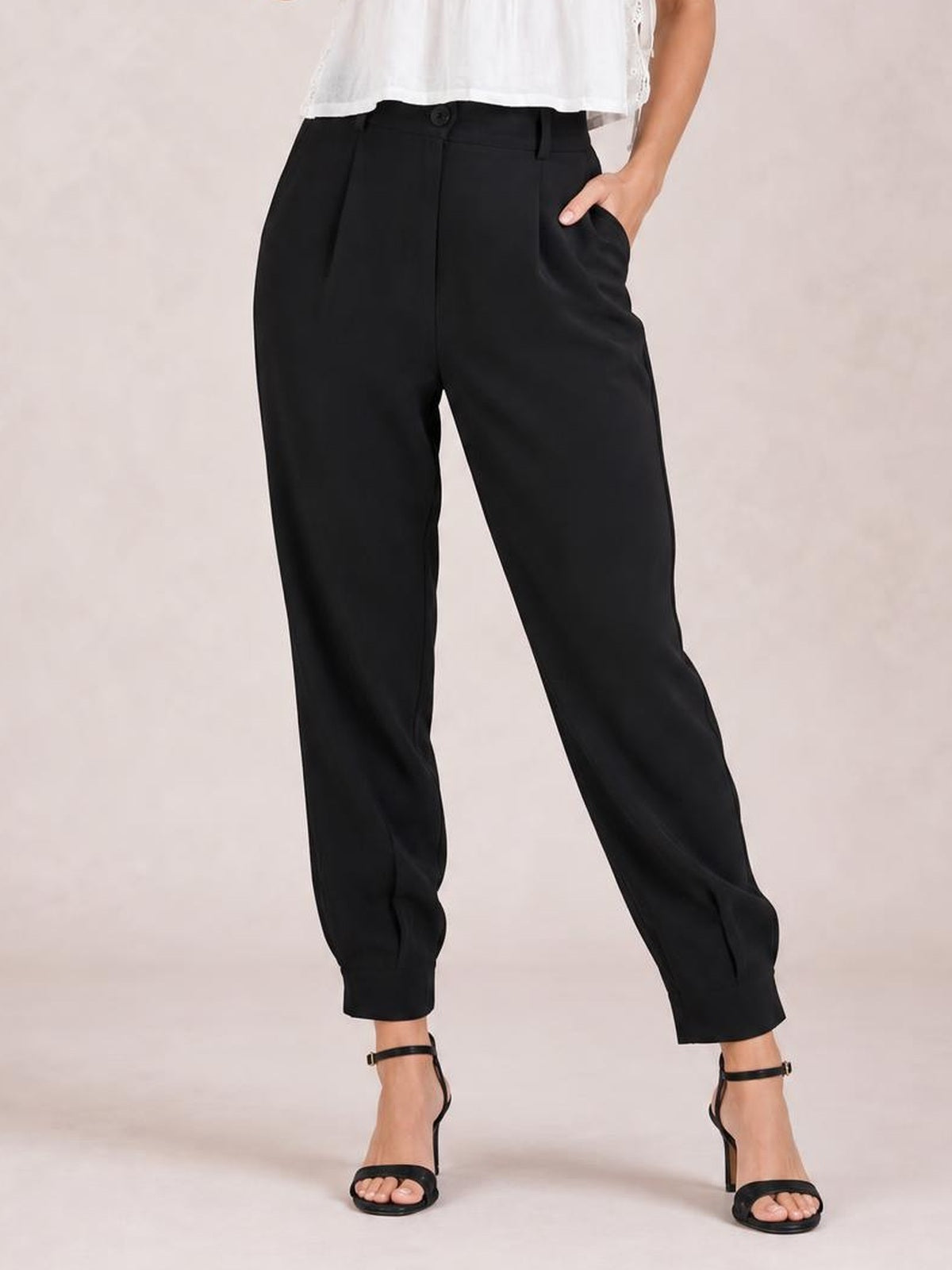 A model wears black high-waist cropped pants with a front button, belt loops, side pockets, a relaxed tapered silhouette, and ankle-length hems.