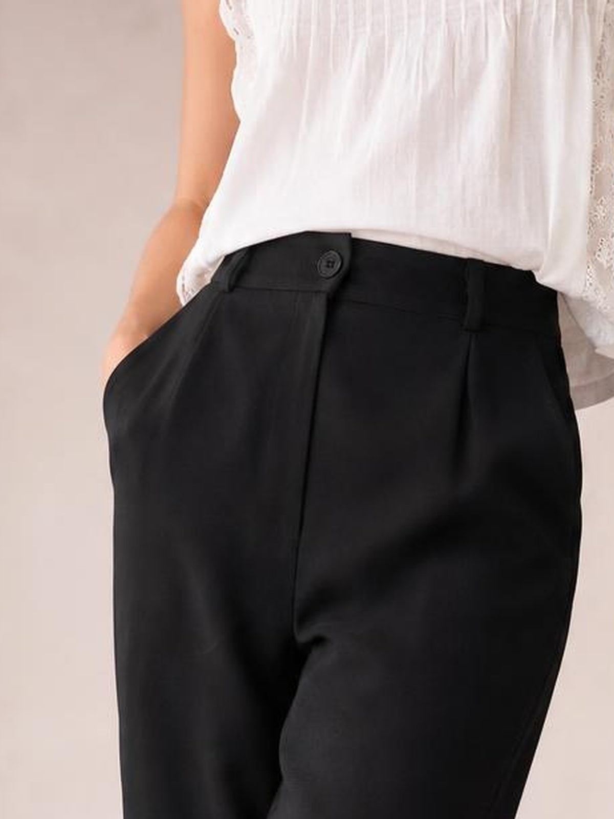 A model wears black high waist cropped pants with a relaxed silhouette, buttoned waistband, belt loops, and spacious side pockets.