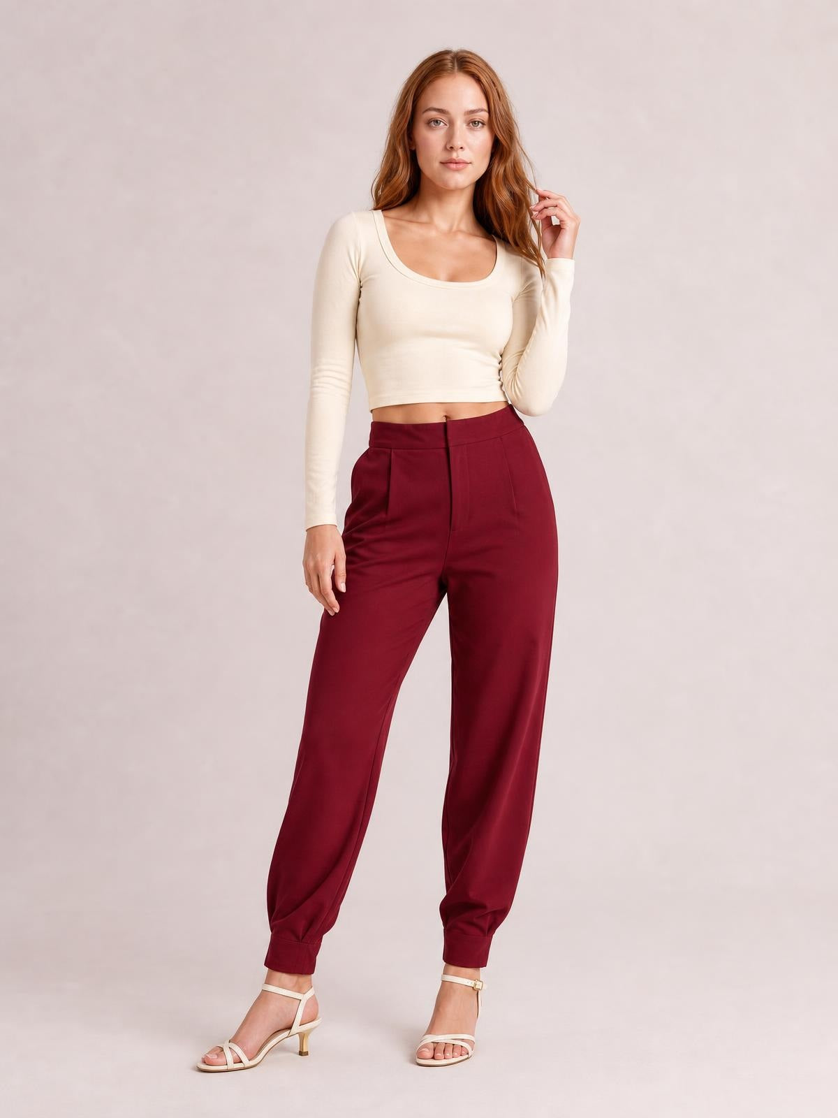 A model poses in burgundy high-waisted cropped pants with a relaxed tapered silhouette, front button closure, side pockets, and gathered ankle cuffs.