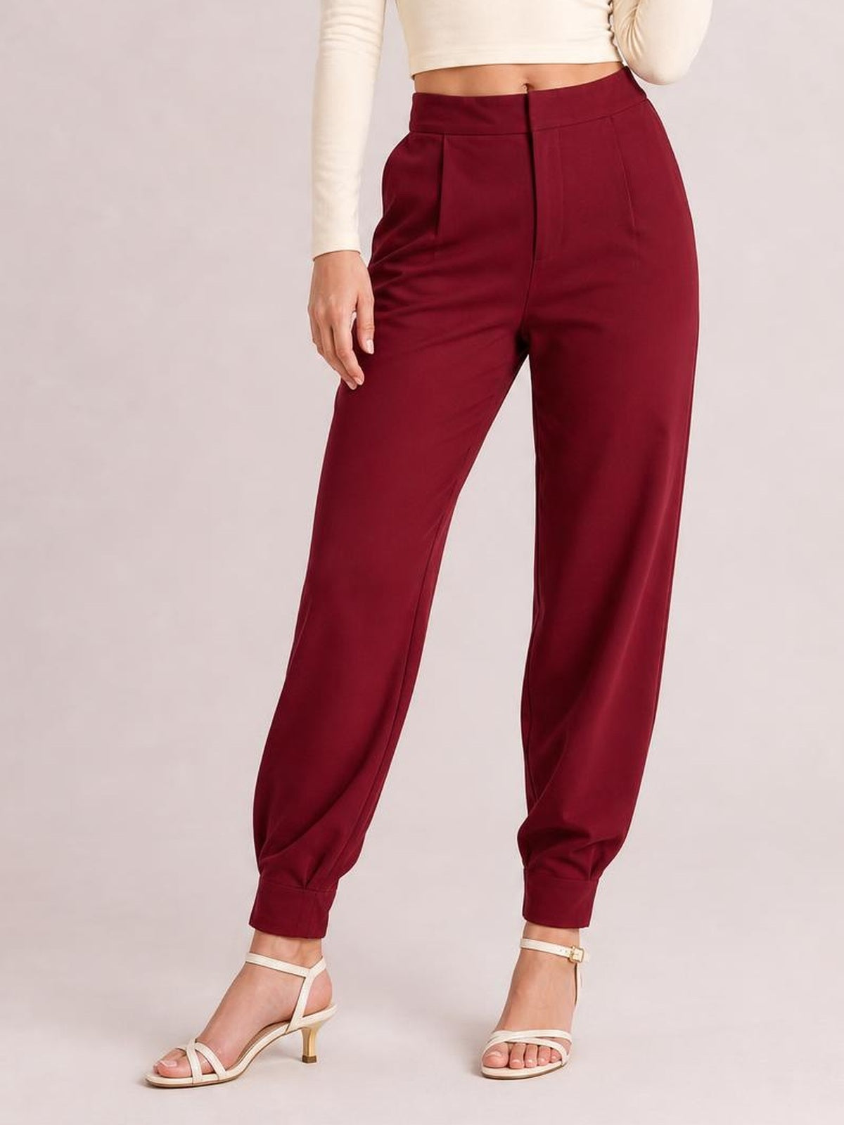 A model wears burgundy high-waist cropped pants with a relaxed jogger silhouette, side pockets, buttoned fly, and fitted ankle cuffs.