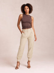 A model poses in high-waist cropped pants in beige, featuring a buttoned front, side pockets, relaxed tapered legs, and gathered ankle cuffs.