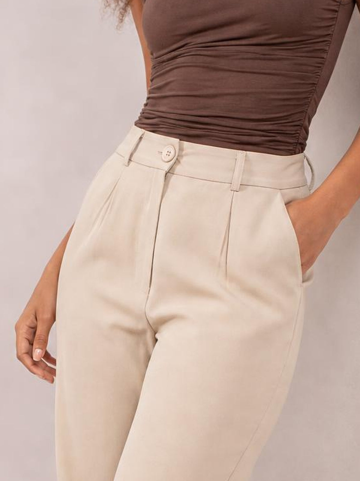 A model poses in cream high-waist cropped pants with a front button closure, belt loops, tailored seams, and practical side pockets.