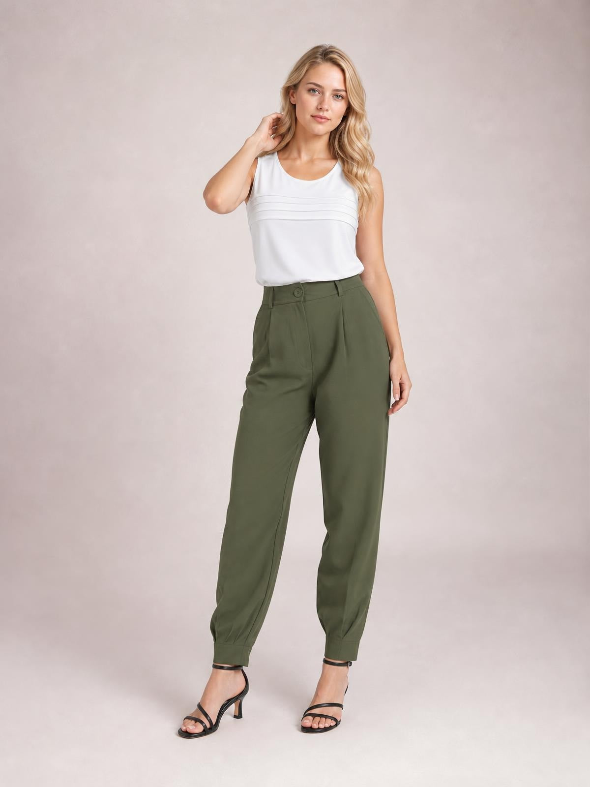 Model poses in high waist cropped olive-green pants with a buttoned waistband, side pockets, front pleats, tapered legs, and ankle cuffs.