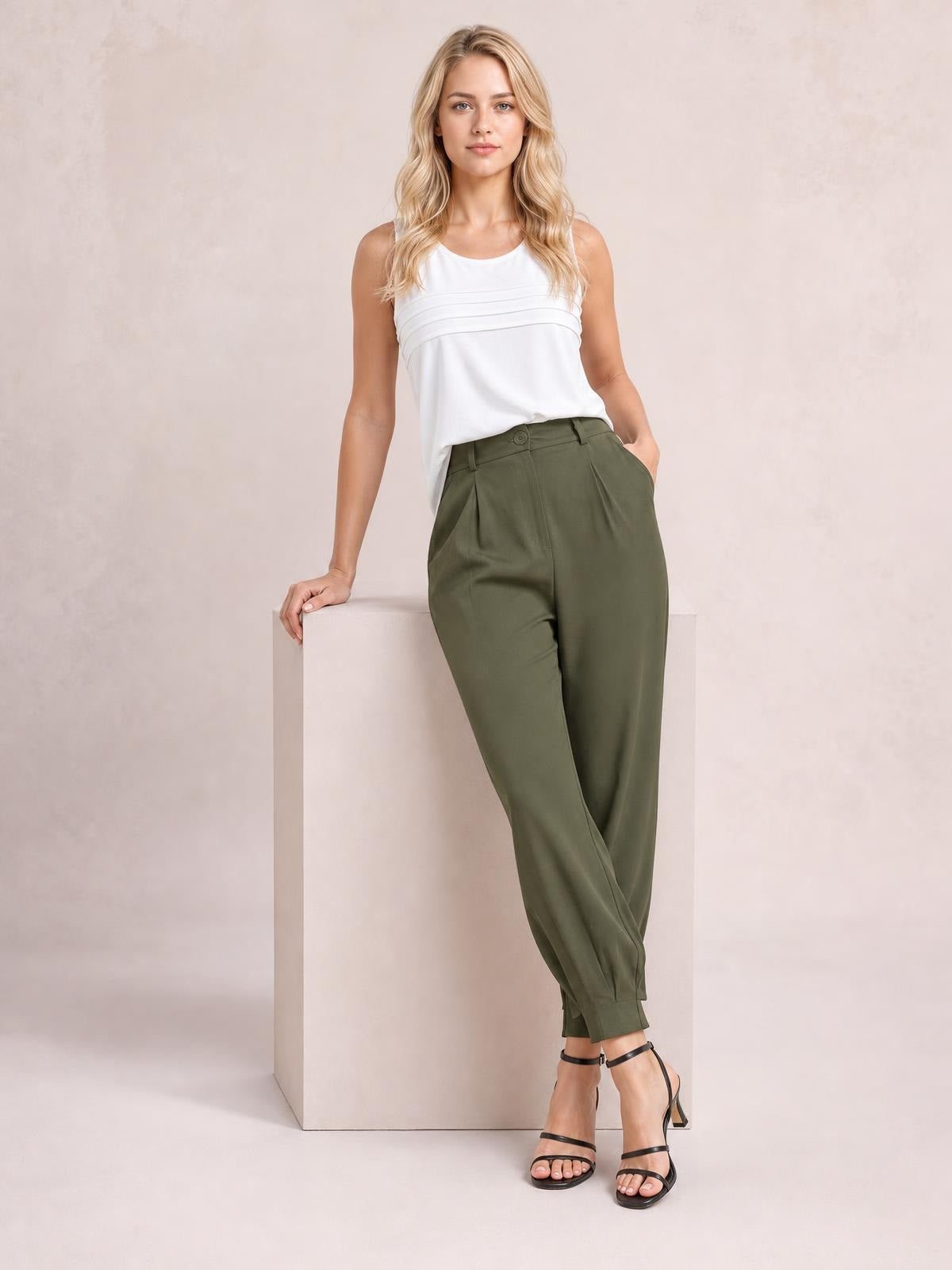 A model poses in olive green high-waist cropped pants with a button closure, belt loops, side pockets, and a relaxed tapered silhouette.