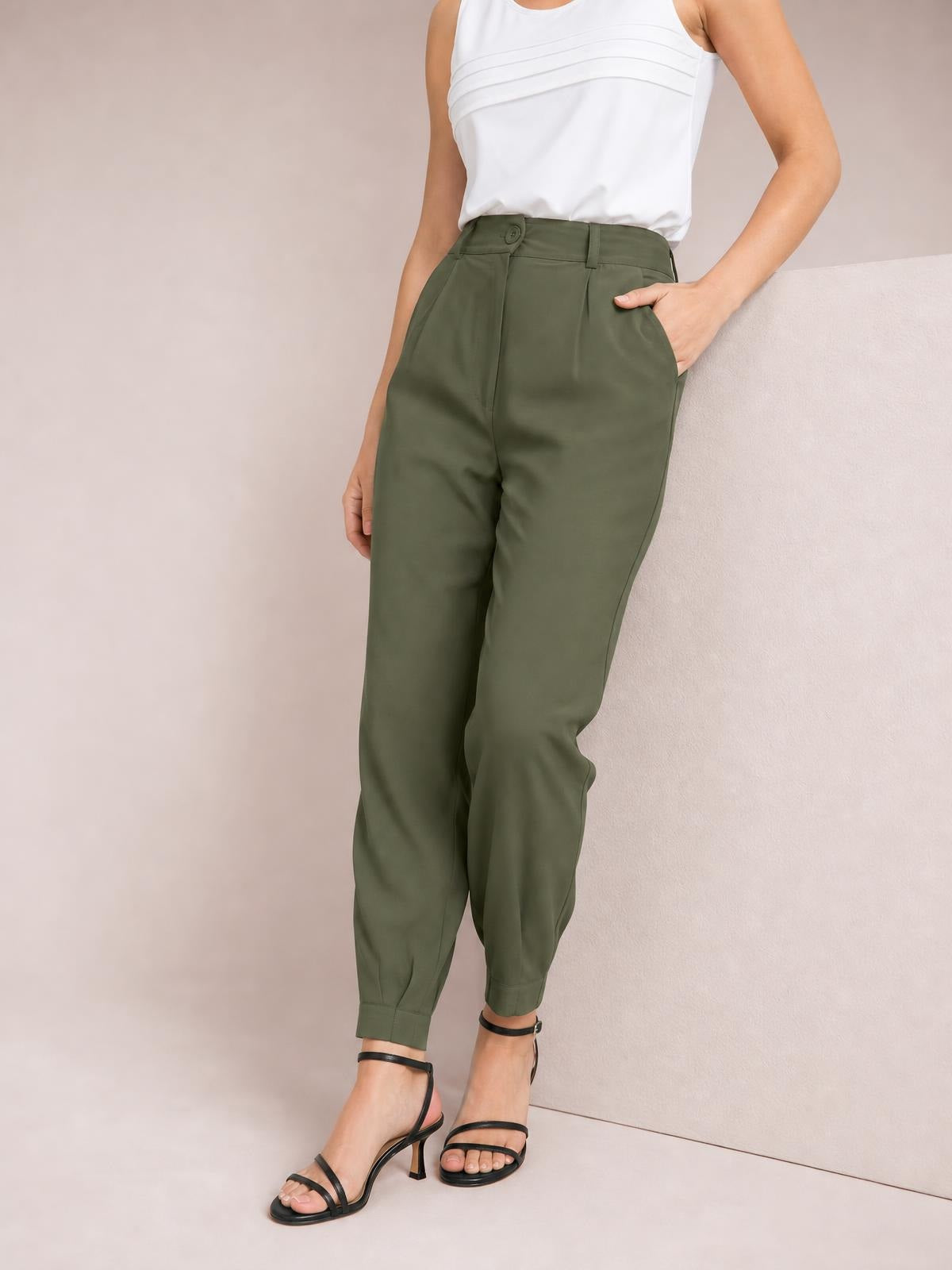 Model standing in olive green high-waisted cropped pants with a tapered silhouette, buttoned waistband, belt loops, front pleats, side pockets, and cuffed hems.