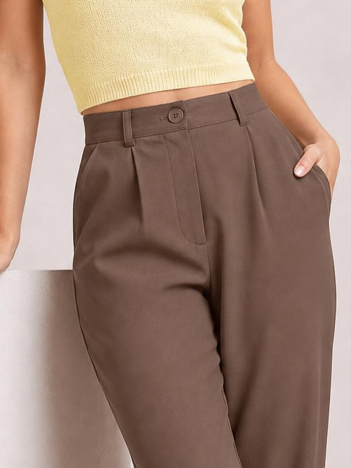 A model wears brown high-waist cropped pants with a buttoned waistband, belt loops, front pleats, and roomy side pockets in a relaxed silhouette.