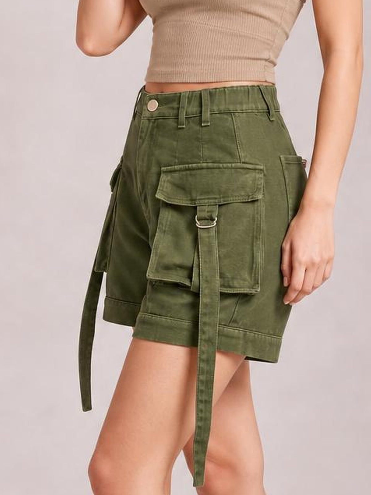 A model stands in olive green high-waist denim cargo shorts with a relaxed silhouette, large flap pockets, belt loops, and long utility straps.