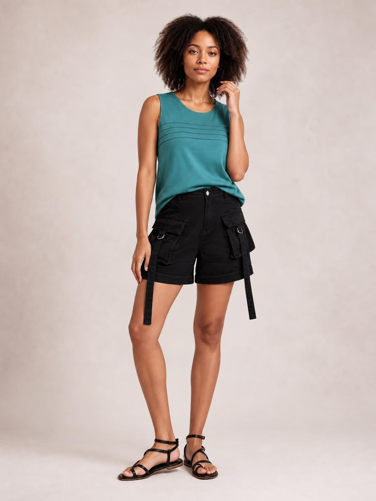 Model poses in black high-waist denim cargo shorts with a cuffed hem, roomy flap pockets, and long side straps.