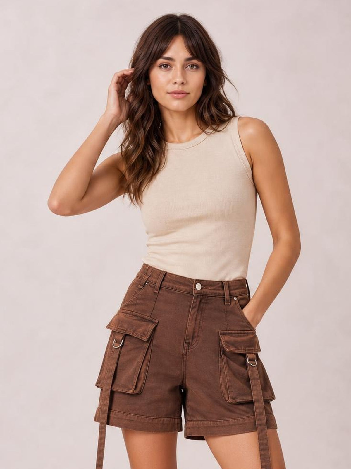 A woman modeling a sleeveless beige ribbed tank top and brown cargo shorts against a light beige studio background.