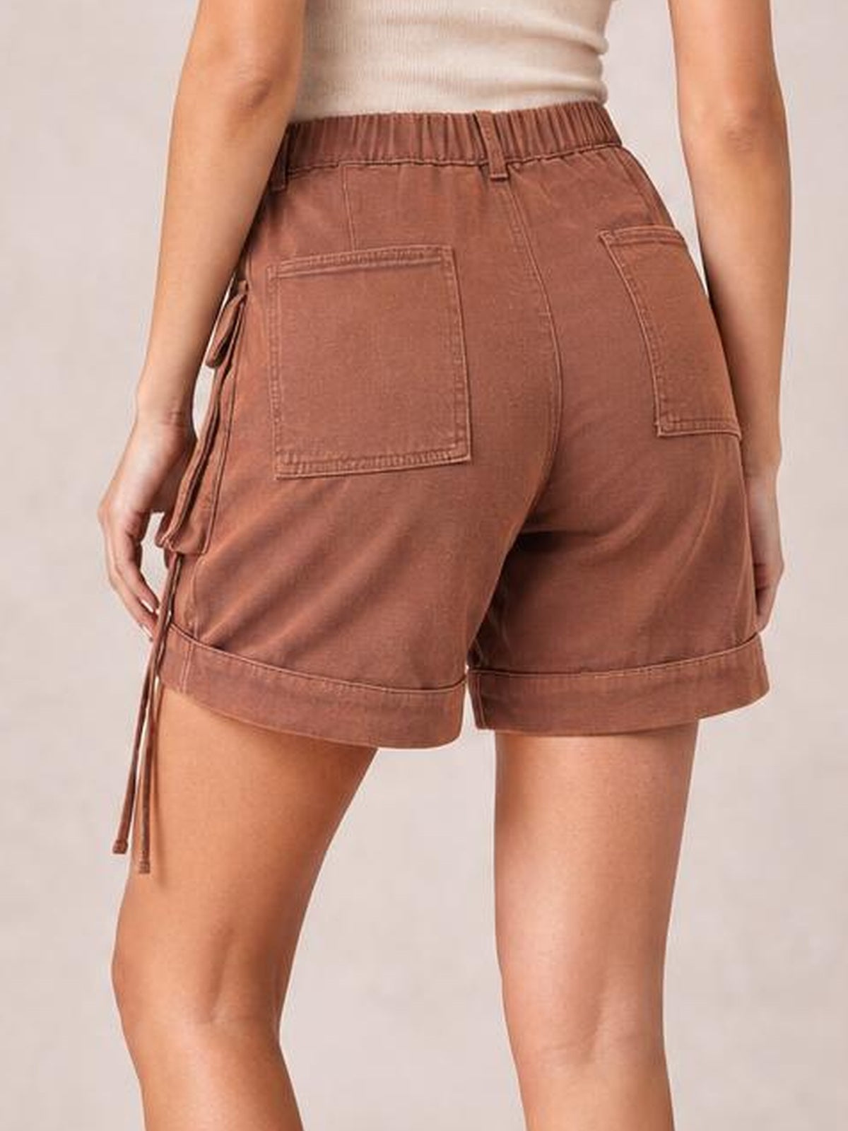 A model stands in a rear view wearing brown high-waist denim cargo shorts with a relaxed silhouette, cuffed hems, and spacious back and side pockets.
