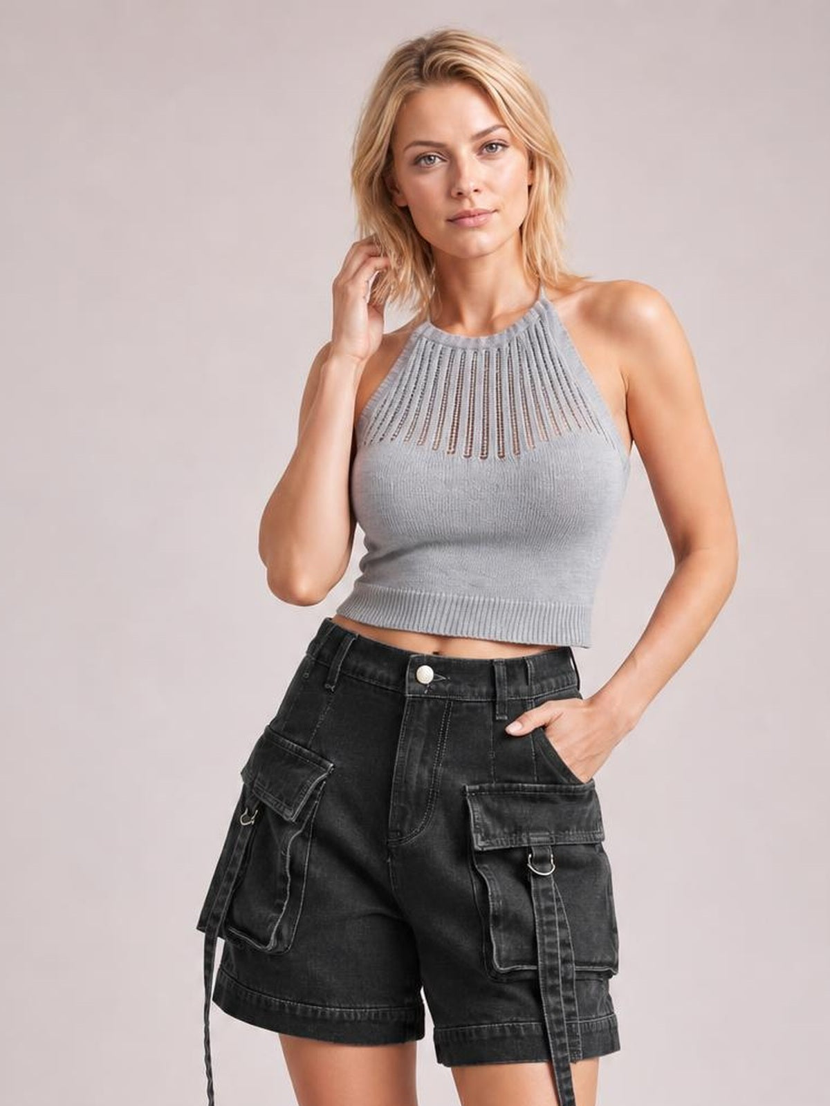 A woman modeling a light gray sleeveless knit crop top with a textured cutout neckline and black cargo shorts against a solid light gray studio background.