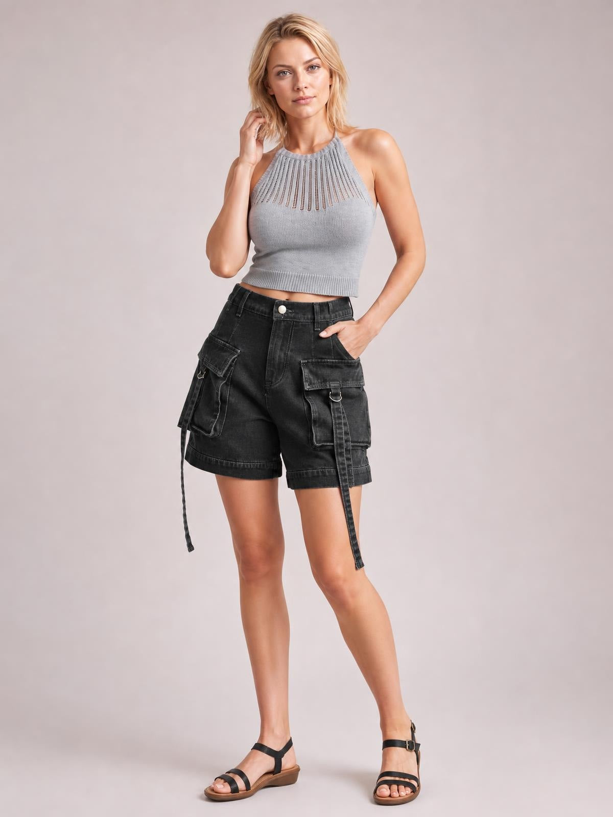 A model poses in black high-waist denim cargo shorts with a relaxed silhouette, multiple utility pockets, cuffed hems, and hanging straps.