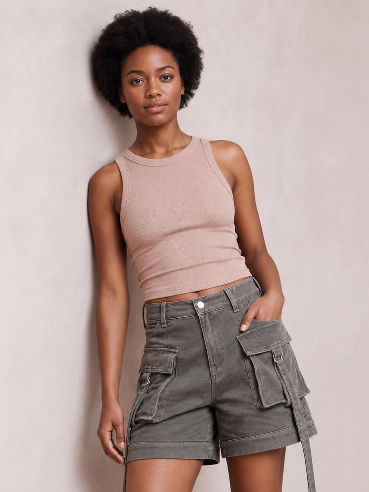 A woman modeling a sleeveless dusty pink ribbed crop top and gray cargo shorts against a neutral beige studio background.