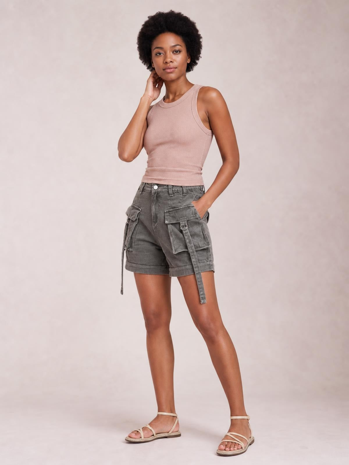A model poses with one hand in the pocket, wearing solid gray high-waist denim cargo shorts with a relaxed silhouette, utility pockets, and cuffed hems.