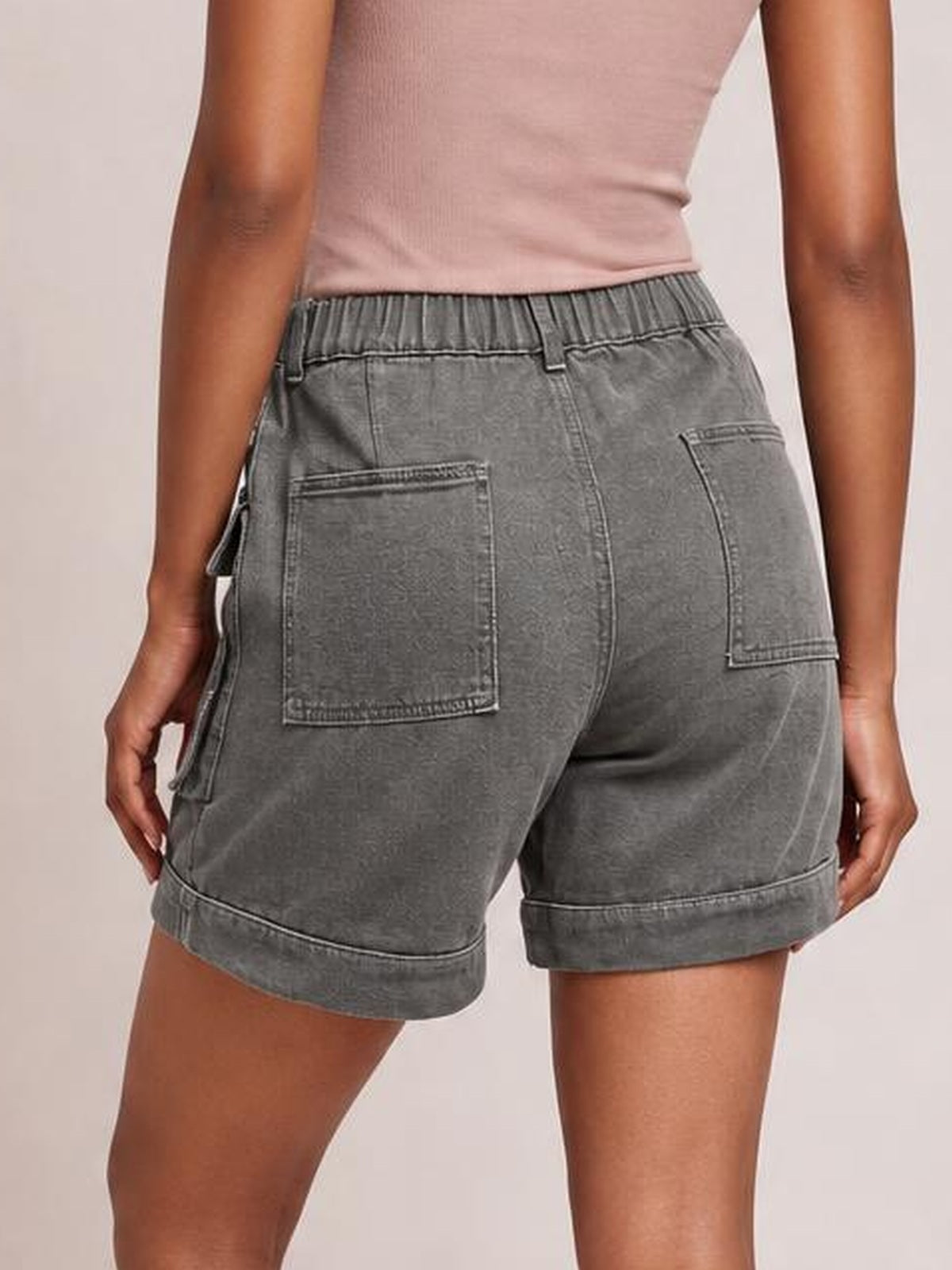 Model shown from behind wearing solid gray high-waist denim cargo shorts with a relaxed fit, multiple patch pockets, belt loops, and cuffed hems.