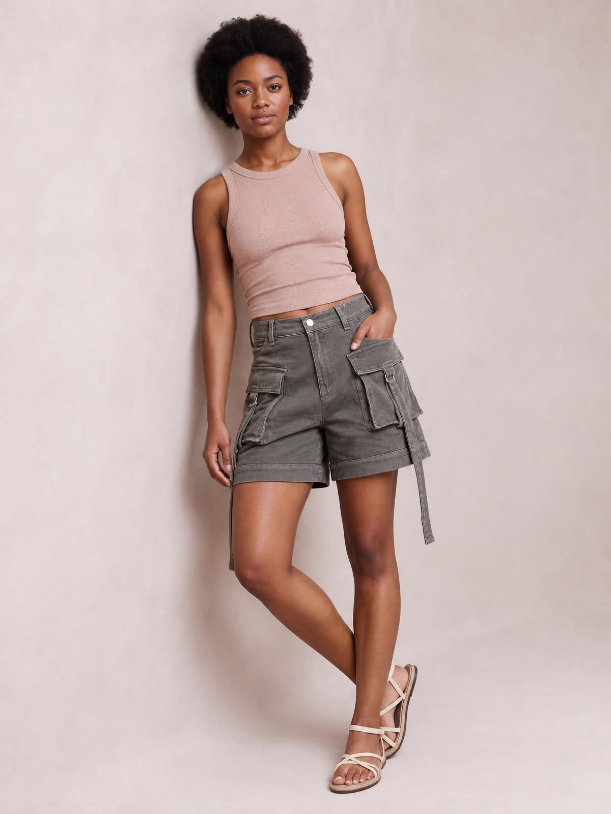 A model poses with one hand in gray high-waist denim cargo shorts featuring a relaxed silhouette, multiple flap pockets, stitched panels, and cuffed hems.