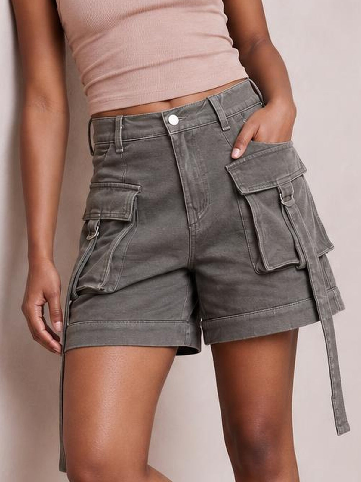 A model poses with one hand in a pocket, wearing solid gray high-waist denim cargo shorts with a structured fit, belt loops, flap pockets, and cuffed hems.
