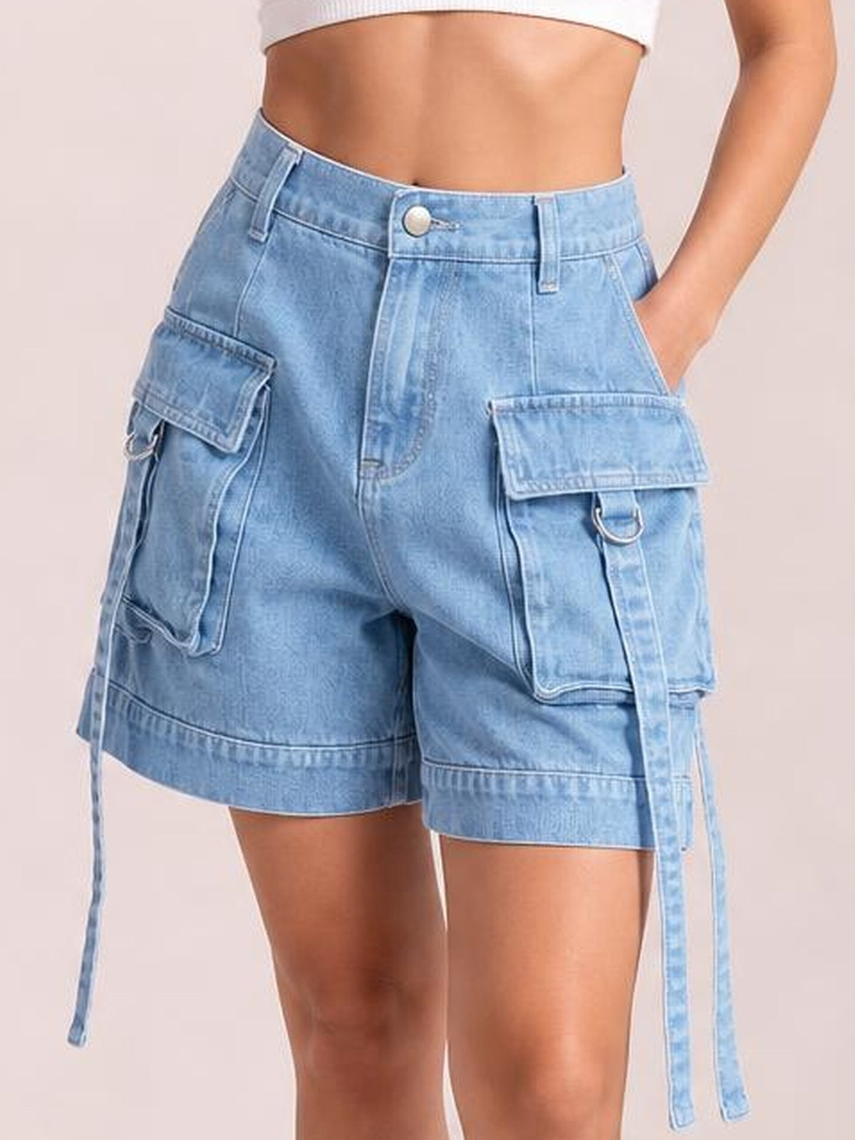 Cropped model wearing light blue high-waist denim cargo shorts with a relaxed silhouette, multiple flap pockets, belt loops, button closure, and hanging straps.