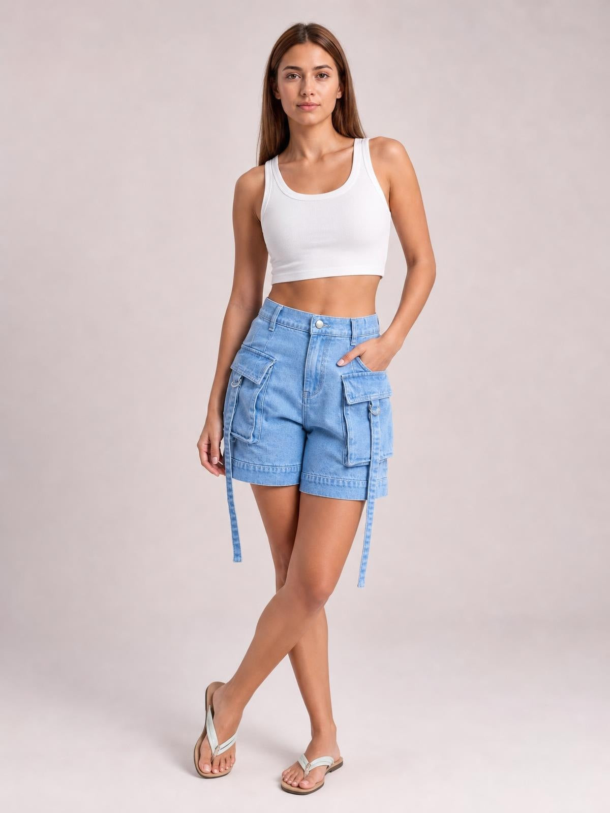 A model poses with crossed legs and one hand in the pocket, wearing light blue high-waist denim cargo shorts with a relaxed fit and multiple flap pockets.