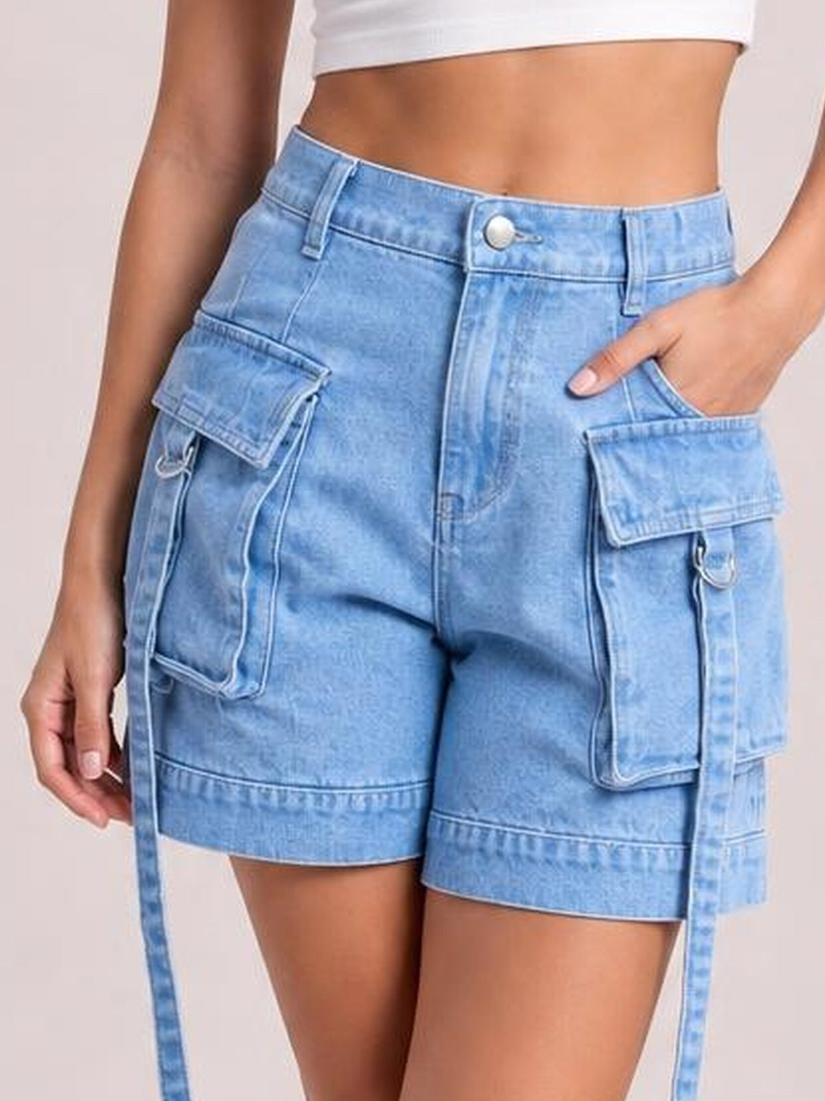 Model wearing light-wash high-waist denim cargo shorts with a tailored fit, belt loops, button closure, multiple flap pockets, and long side straps.