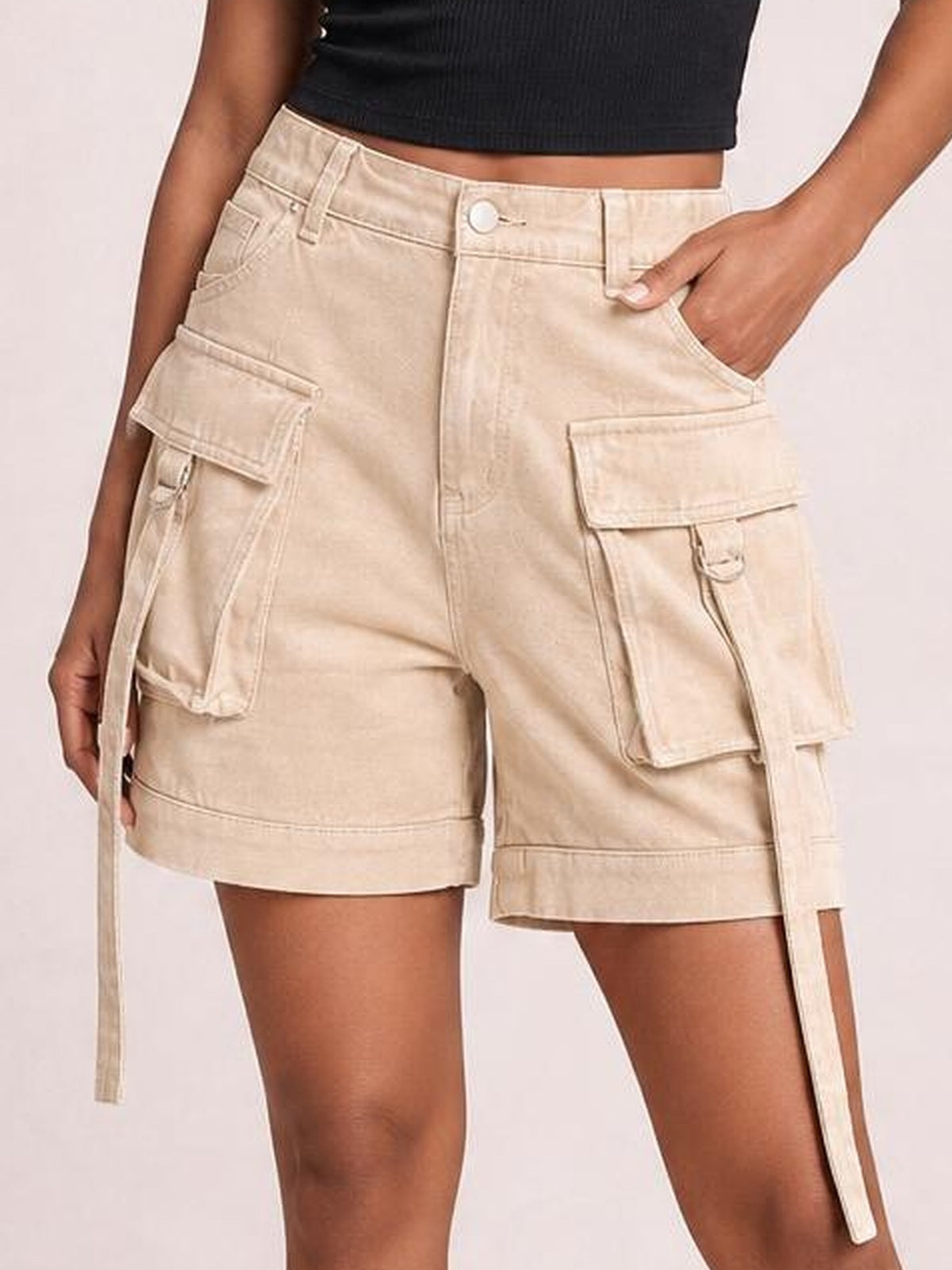 Model wears solid beige high-waist denim cargo shorts with a structured relaxed fit, belt loops, button closure, flap pockets, and long utility straps.