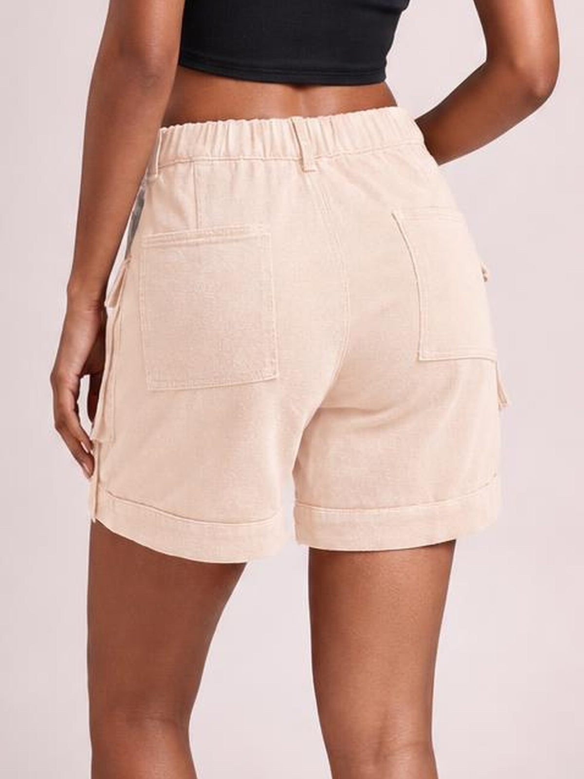 Model poses in light cream high-waist denim cargo shorts with a gathered waistband, relaxed straight-leg silhouette, and roomy utility pockets.