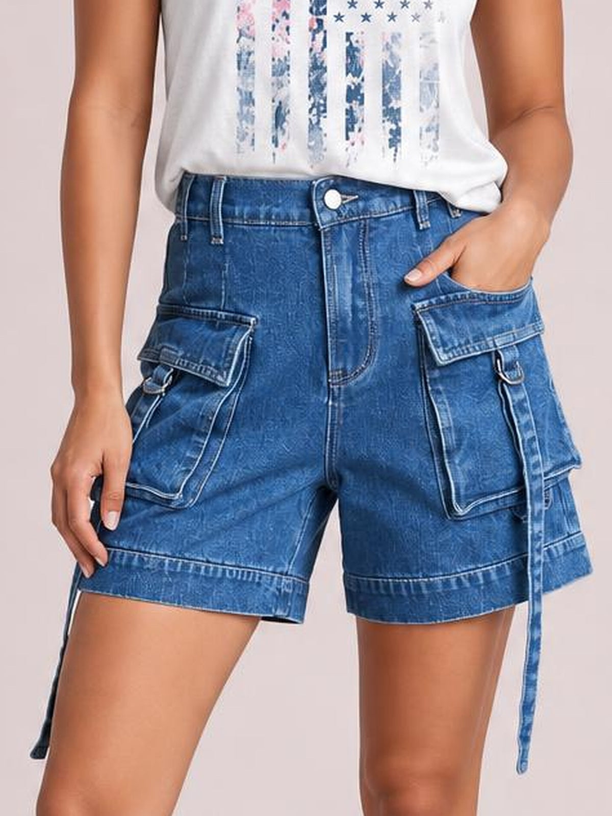 A model wears blue high-waist denim cargo shorts with a relaxed silhouette, belt loops, button fly, and multiple flap pockets, one hand tucked inside.