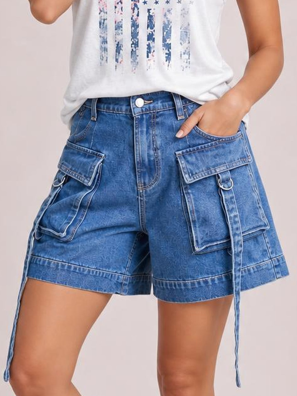 Model poses with one hand in the pocket, wearing blue high-waist denim cargo shorts with a relaxed fit, belt loops, button fly, and multiple flap pockets.