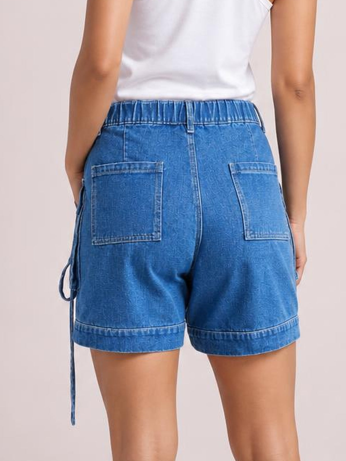 Model shown from the back wearing blue high-waist denim cargo shorts with a relaxed fit, large patch pockets, side cargo pockets, and rolled hems.