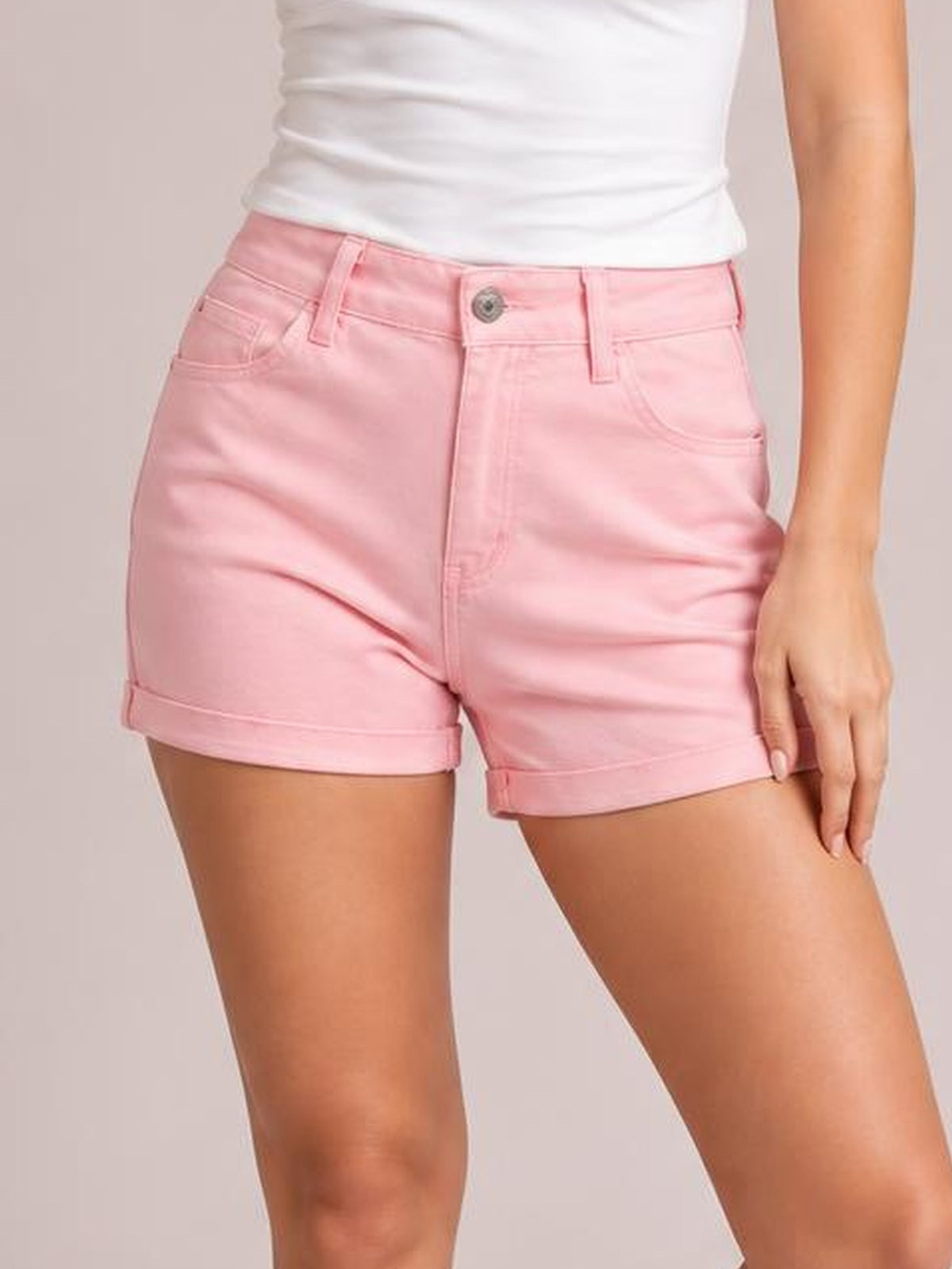 A model wears pink high-waist denim shorts with a fitted silhouette, button closure, belt loops, front pockets, and neatly cuffed hems.