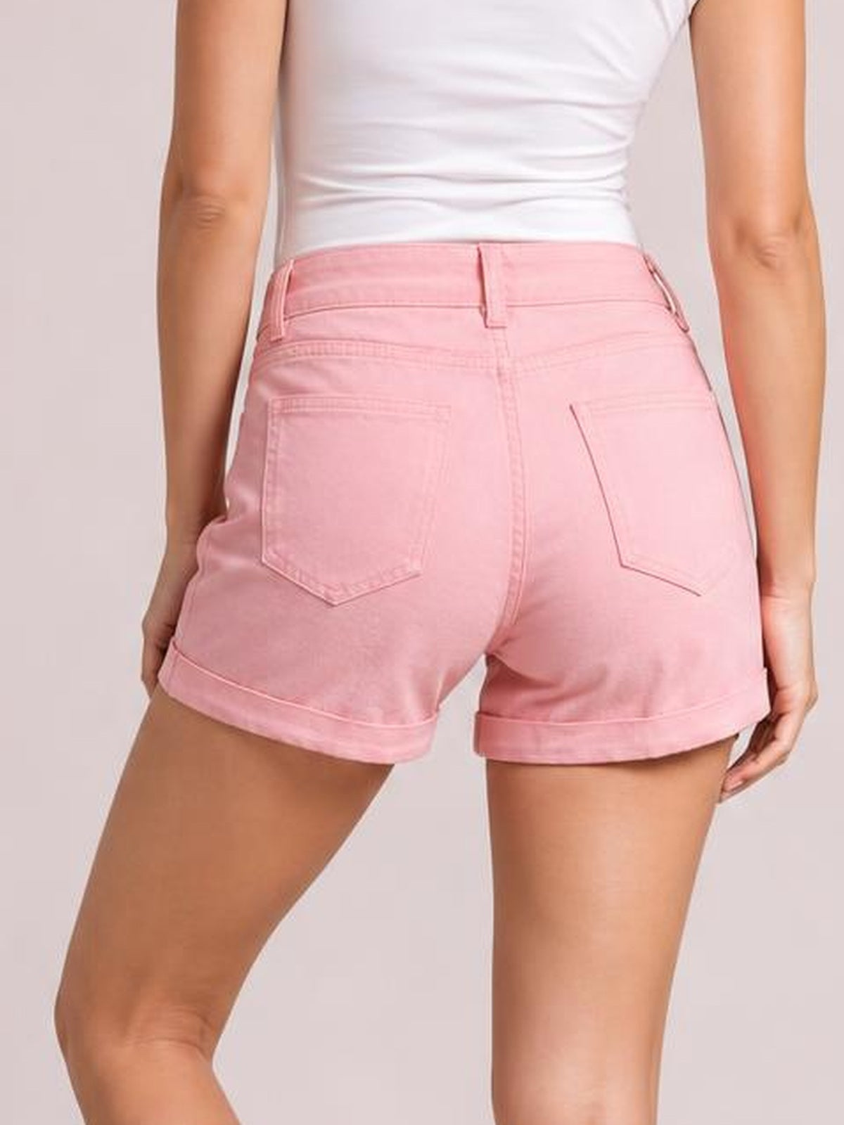 Model shown from the back wearing pink high-waist denim shorts with belt loops, two patch pockets, a fitted silhouette, and cuffed hems.