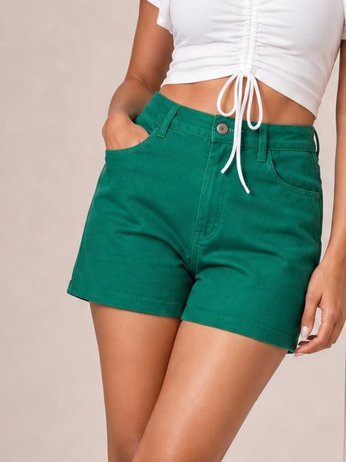 Model wears emerald green high waist denim shorts with a button closure, belt loops, front pockets, stitched seams, and a straight short-leg silhouette.