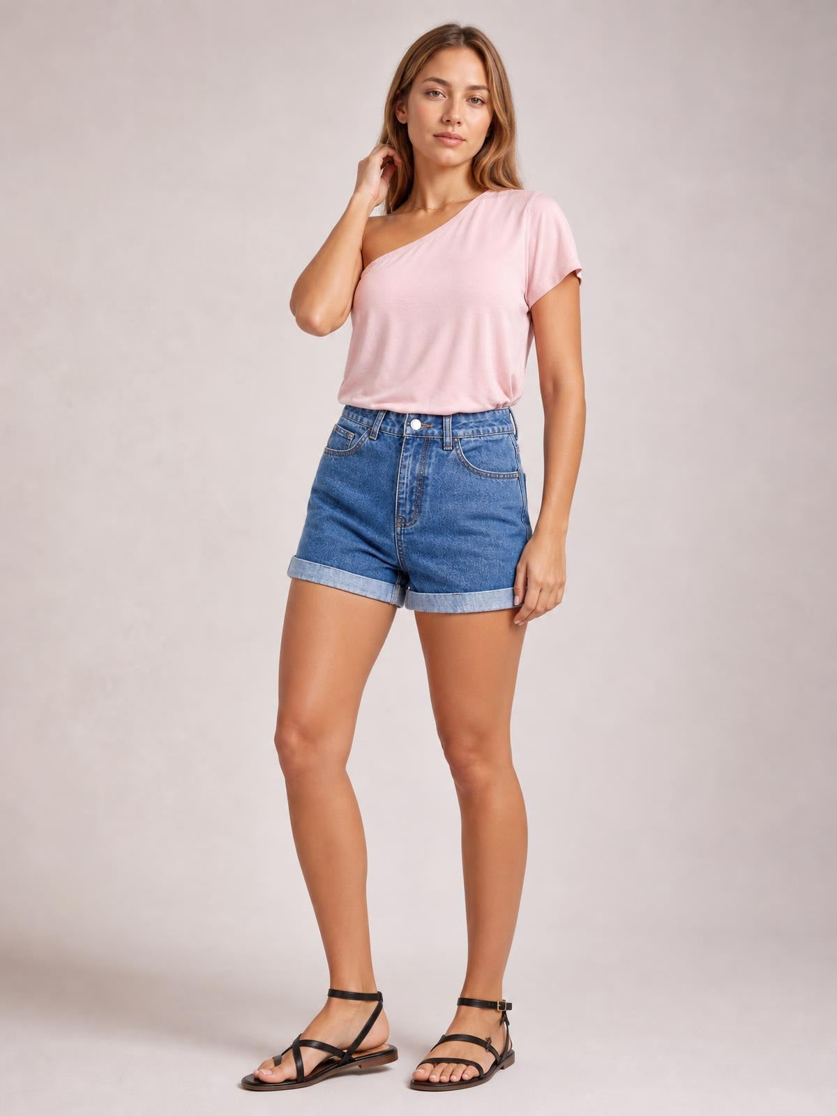 A model stands with one hand near her hair, wearing blue high-waist denim shorts with front buttons, pockets, a structured fit, and rolled cuffs.