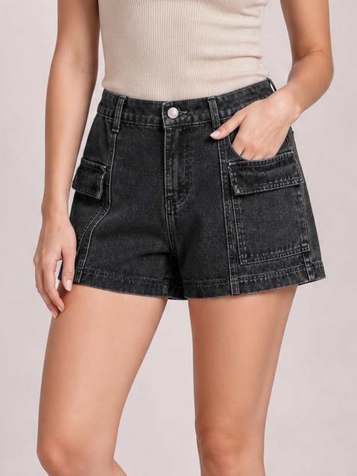 Model wearing high-waist black denim shorts with a structured silhouette, button closure, contrast seam detailing, and multiple front utility pockets.