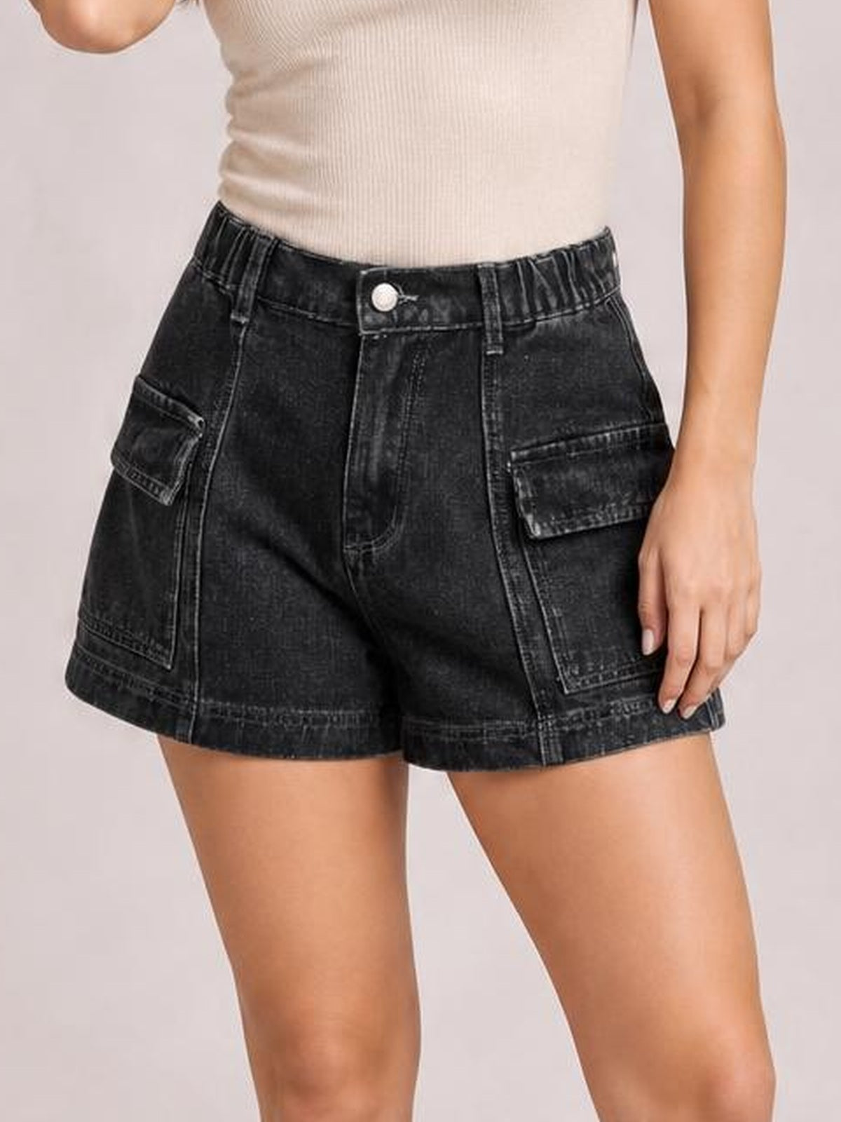 Model wears black high-waist denim shorts with a structured silhouette, button closure, seam details, belt loops, and large flap pockets.
