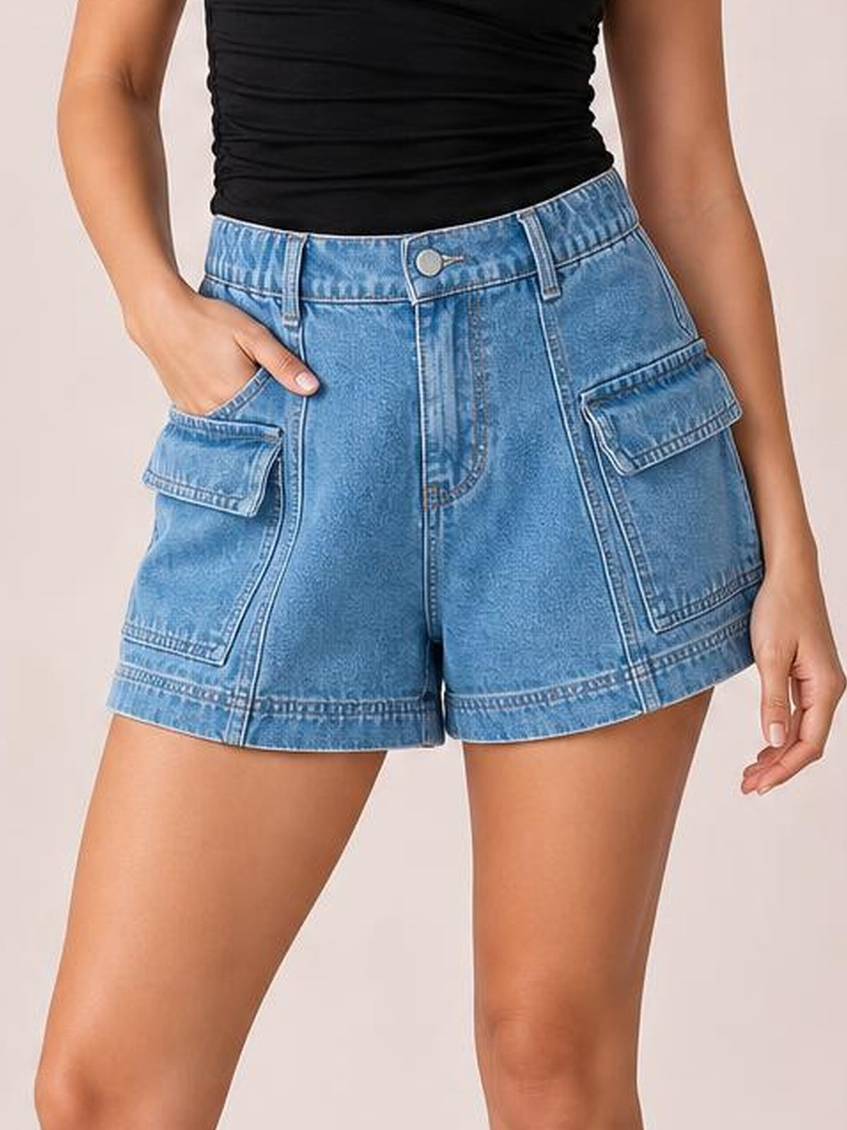 Model wears light blue high-waist denim shorts with a structured relaxed silhouette, button closure, belt loops, seam detailing, and large flap pockets, posing with one hand tucked in a pocket.