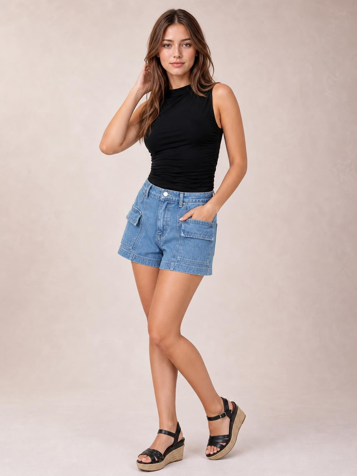 A model poses with one hand in the pocket, wearing light blue high-waist denim shorts with seam detailing, belt loops, and large patch pockets.