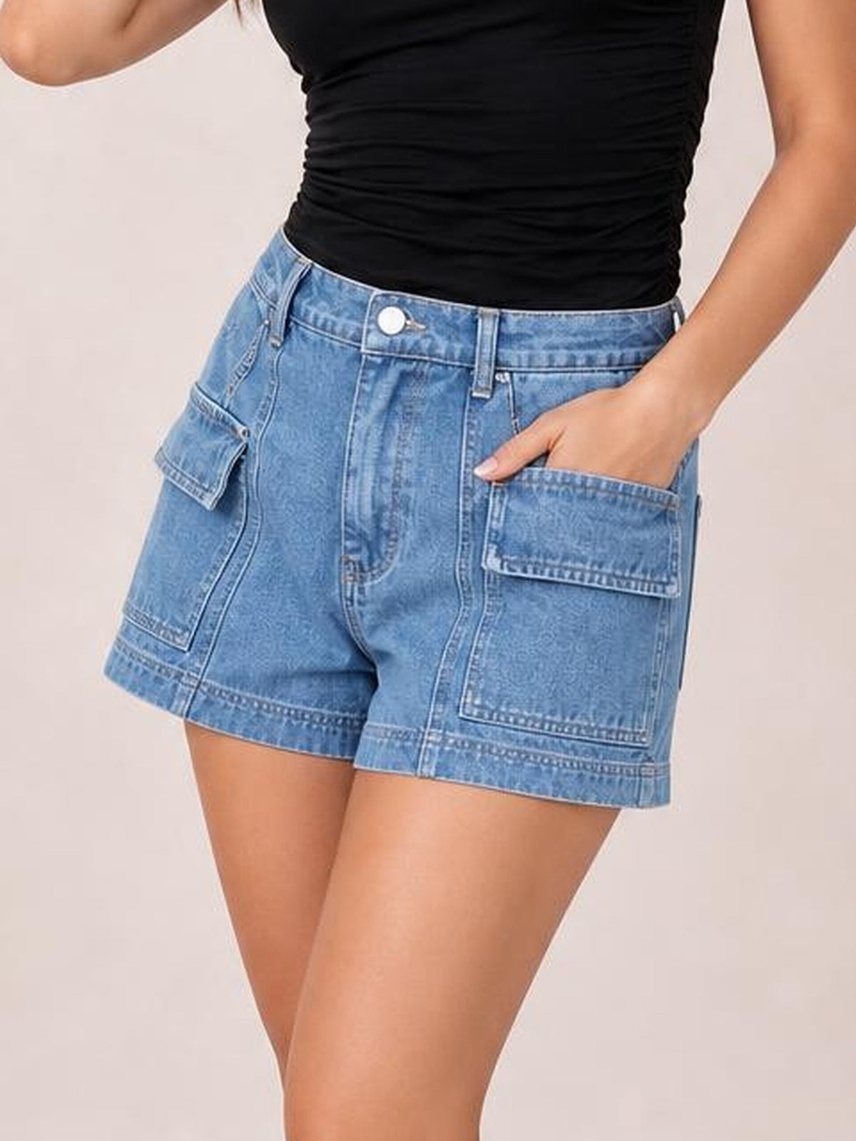Model wearing light blue high waist denim shorts with belt loops, button closure, seam detailing, and multiple utility pockets in a relaxed silhouette.