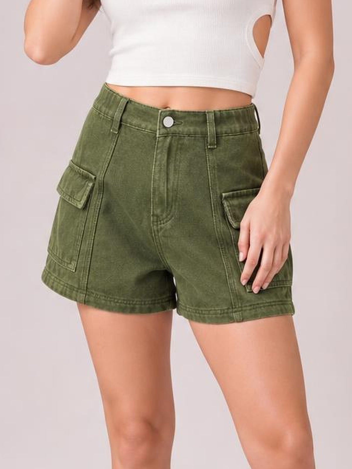 Model standing in olive green high-waist denim shorts with a button closure, belt loops, seam detailing, and flap cargo pockets.